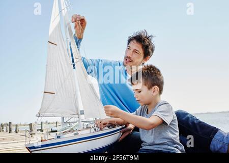 Vater und Sohn bereiten gemeinsam ein Spielzeug-Segelboot vor, während sie sitzen pier Stockfoto
