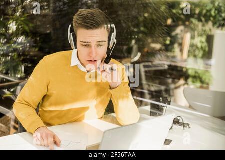 Junger Profi mit Kopfhörern, der zu Hause an einem Geschäftstreffen teilnimmt Büro Stockfoto