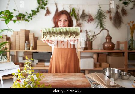 Frau hält ein Stück Bio-Seife, während sie in der Werkstatt steht Stockfoto