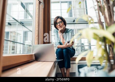 Unternehmerin mit Smartphone, das beim Sitzen wegschaut Büro Stockfoto