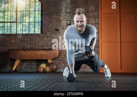 Lächelnder männlicher Athlet trainiert mit Hanteln im Fitnessstudio Stockfoto