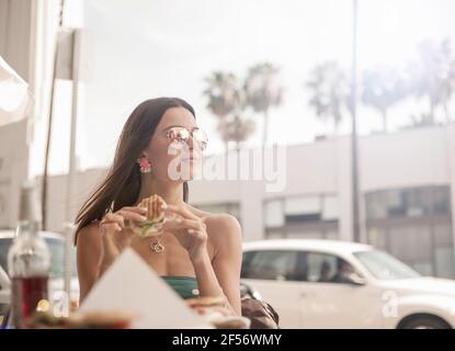 Wunderschöne Frau, die beim Burger-Essen im Restaurant wegschaute Stockfoto