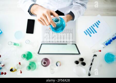 Wissenschaftler, der im Labor eine Flasche über dem Laptop hält Stockfoto