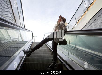 Frau, die sich am Geländer lehnte, während sie auf der Rolltreppe gegen den Himmel stand Stockfoto