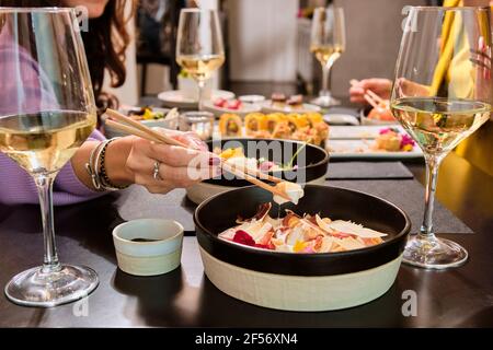Frau mit Essstäbchen essen, während sie mit Freunden sitzt Restaurant Stockfoto