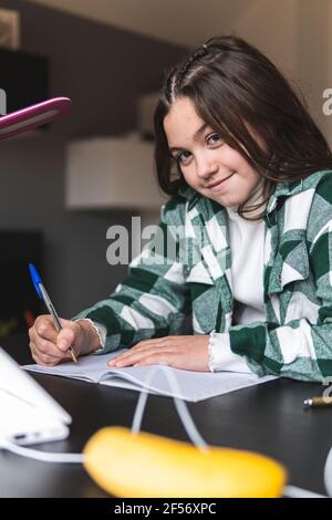 Lächelndes Mädchen, das am Tisch im Wohnzimmer studiert Stockfoto