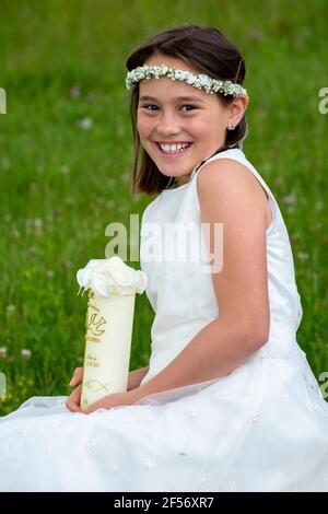 Fröhliches Mädchen in weißem Kleid mit Kerze am Kommunionstag Stockfoto