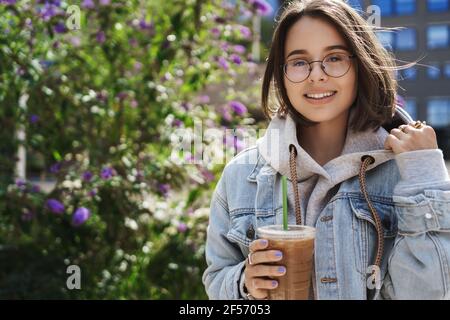 Lifestyle, Universität und Bildungskonzept. Nahaufnahme Porträt von glücklich niedlichen queer Mädchen genießen Frühlingstage, Schluck Kaffee zum Mitnehmen und lächelnde Kamera Stockfoto