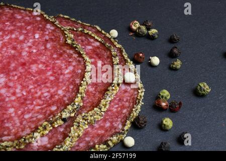 Makro Nahaufnahme von Scheiben französisch frische Salami mit gemischtem Pfeffer Kruste mit Pfefferkörnern auf schwarzem Schiefersteinbrett Stockfoto