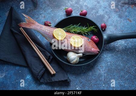 Stillleben ein Fisch auf einer Pfanne mit Zitrone und Knoblauch mit Hintergrund Stockfoto