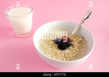 Frühstück: Haferflocken mit Beeren und Milch im Glas auf dem rosa Hintergrund Stockfoto