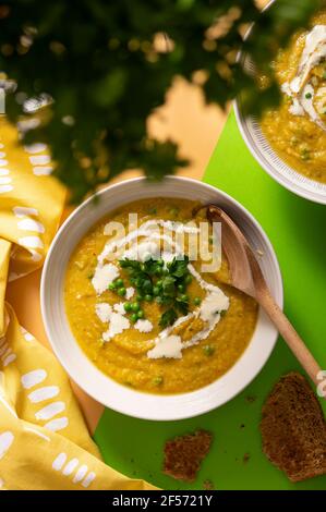 Vegetarische Butternut-Kürbis-Sahne-Suppe garniert mit frischen grünen Erbsen Und Petersilienblätter auf leuchtend gelbem und grünem Hintergrund Stockfoto
