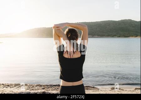 Unkenntliche Frau macht Stretching-Übungen für Arme vor dem Meer Blick auf den Horizont mit Sonnenlicht. Stockfoto
