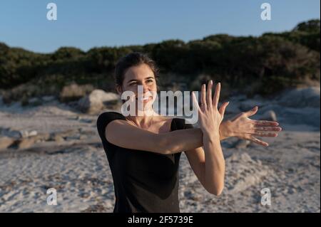 Junge Frau in Sportbekleidung tun Stretching-Übungen für Hals und Arme an der Küste mit entspanntem Smiley nach vorne schauen Gesicht beim Atmen frisch A Stockfoto