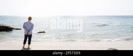 Horizontales Banner mit unkenntlichen Mann in Business-Anzug stehend am Ufer in einem schönen italienischen Strand Blick auf den Horizont. Meditation, Stockfoto