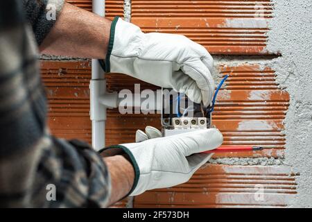 Elektriker bei der Arbeit führt das Elektrokabel in die Klemme eines Leistungsschalters einer elektrischen Anlage in Wohngebäuden ein. Sicheres Arbeiten mit PR Stockfoto