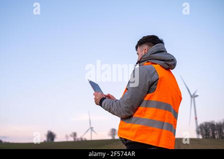 Der Windmühleningenieur führt die Wartung und Reparatur von Windenergieanlagen mithilfe eines Tabletts in der orangefarbenen vesta durch. Stockfoto