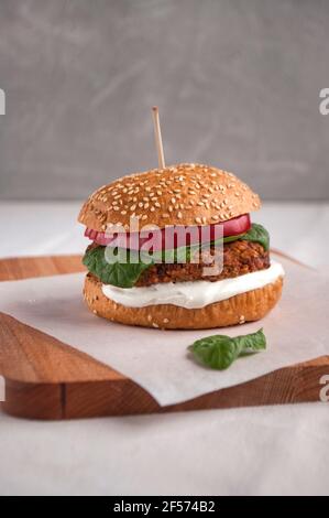 Veganer Burger mit roten Bohnen, rotem Pfeffer, Spinat und weißem Joghurt. Frischer, köstlicher vegetarischer Burger auf einem Schneidebrett. Stockfoto