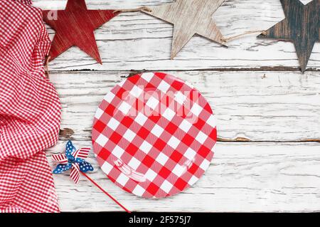 Teller auf einem weißen Holzpicknicktisch mit zerknitterter roter und weißer Gingham-Tischdecke und Holzsternen. Stockfoto