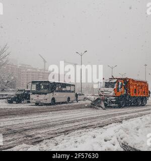 Bus und andere Autos schleppen während des Schneesturms auf schneebedeckter Straße Während Schneepflug den Schnee löscht Stockfoto