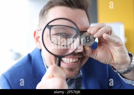 Der Mensch schaut durch die Lupe und hält Bitcoin in seinem Hand Stockfoto