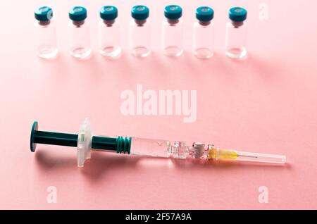 Spritze mit mehreren medizinischen Fläschchen zur Injektion auf rosa Hintergrund. Stockfoto