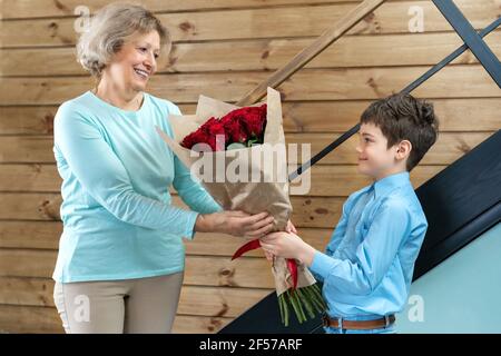 Ein Junge schenkt seiner Großmutter bei einem Familienfest Blumen. Das Konzept der warmen Beziehungen zwischen der älteren und der jüngeren Generation in der Familie. Stockfoto
