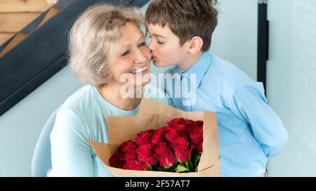 Ein Junge küsst seine Großmutter auf die Wange und schenkt ihr Blumen zu ihrem Geburtstag, Jubiläum, Muttertag. Das Konzept der Altenpflege relativ Stockfoto