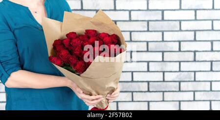 Ein Mädchen hält einen Strauß roter Rosen in einem Bastelpapier-Paket. Das Mädchen erhielt einen Blumenstrauß als Geschenk für ihren Geburtstag, Valentinstag, anni Stockfoto