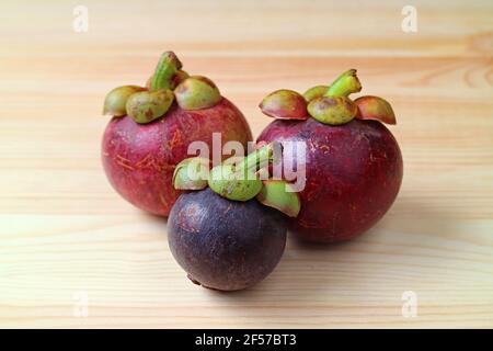 Drei frische reife Purple Mangostan Früchte als "Königin bekannt Von Früchten' auf einem hölzernen Hintergrund Stockfoto