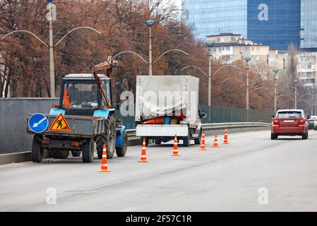 Ein Team von Straßendienstmitarbeitern auf einem alten kommunalen Traktor und einem LKW umschließen einen Straßenabschnitt mit orangefarbenen Kegeln für die anschließende Reinigung. Stockfoto