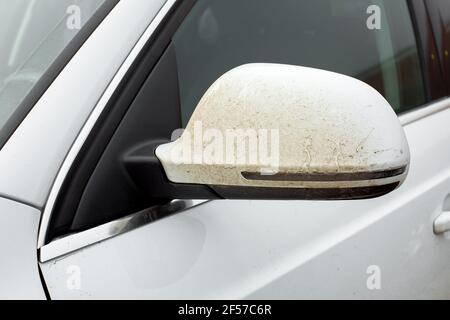 Rückspiegel bedeckt mit einer Schicht von haftendem Schmutz zu einem weißen schmutzigen Auto mit Blinkern auf der Außenspiegel Körper Nahaufnahme. Stockfoto