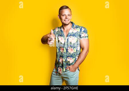 Positive männliche im trendigen Outfit lächelnd und wies auf die Kamera beim Stehen vor gelbem Hintergrund Stockfoto