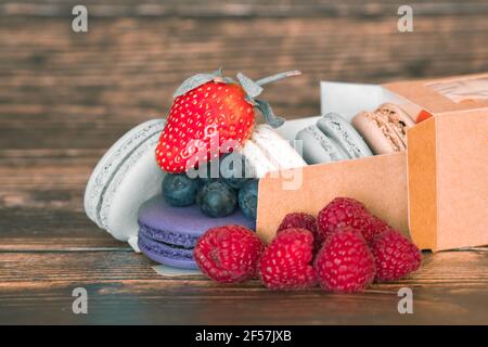 Nahaufnahme einer Schachtel handgemachter Plätzchen - Makronen und frische wilde Heidelbeeren und Himbeeren. Stockfoto