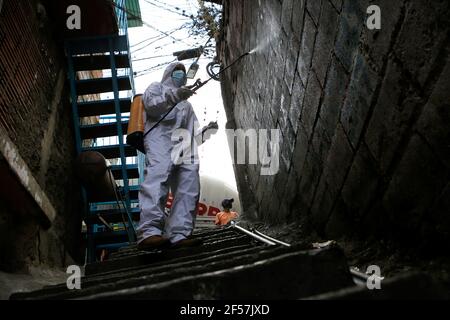 Sucre, Venezuela. März 2021, 24th. Ein Angestellter des Bürgermeisters von Sucre sprüht eine Lösung aus Hypochlorit und Wasser, um die Ausbreitung von Covid-19 in einem schmalen Durchgang im Viertel Cuatricentenario des beliebten Viertels Petare zu verhindern. Kredit: Jesus Vargas/dpa/Alamy Live Nachrichten Stockfoto