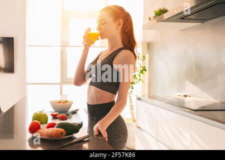 Athletische junge rothaarige Frau in der Küche trinkt ein Glas Fruchtsaft zentrifugiert Stockfoto