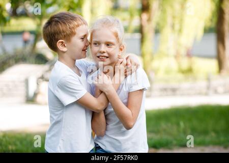 Der Junge flüstert dem Mädchen ein Geheimnis ins Ohr. Kinder für einen Spaziergang im Park. Stockfoto