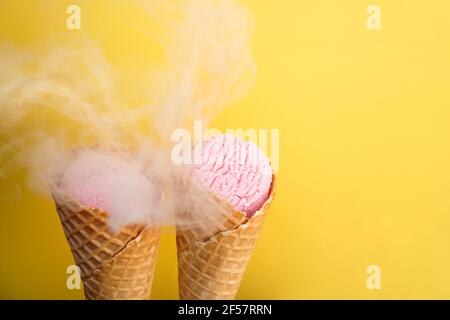Leckeres Eis in einem Waffelkegel auf einem gelben Hintergrund mit Rauch bedeckt Stockfoto
