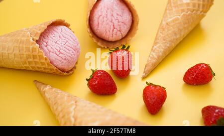 Erdbeereis in einem Waffelkegel. Eis und Beeren auf einem gelben Stockfoto