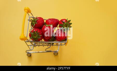 Frische Erdbeeren in einem Einkaufswagen auf einem hellen Gelb Hintergrund Stockfoto