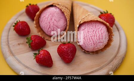 Erdbeereis in einem Waffelkegel. Eis und Beeren auf einem gelben Stockfoto