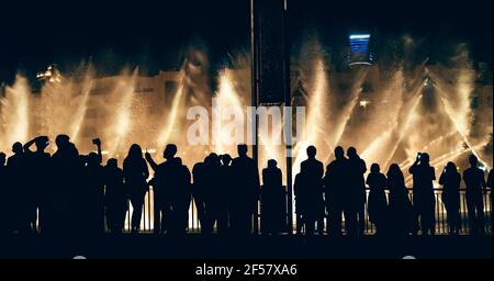 Singende und tanzende Springbrunnen in Dubai mit Silhouetten der Menge von Touristen beobachten Show und fotografieren, horizontale Panoramabild. Stockfoto