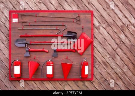 Feuerwehrschild mit Feuerlöschgerät und Sicherheitswerkzeug, hängender Satz von Kampfwerkzeugen an einer Holzwand, niemand. Stockfoto