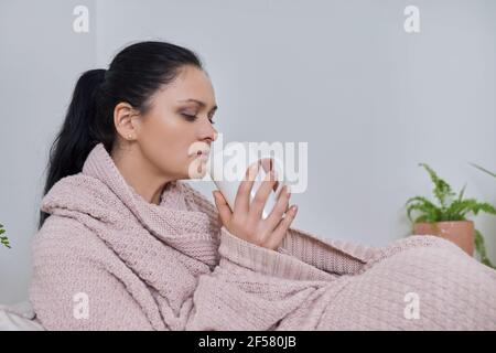 Schöne Frau sitzt zu Hause unter gestrickten warmen Decke mit tasse Tee Stockfoto