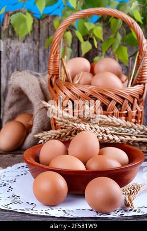 Eier in einer Holzschüssel mit einem kleinen Korb und Leinensack Hintergrund Stockfoto