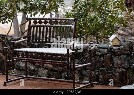 Schneebedeckte antike Schaukelbank, umgeben von einer Felswand Und Stechpalmen Stockfoto