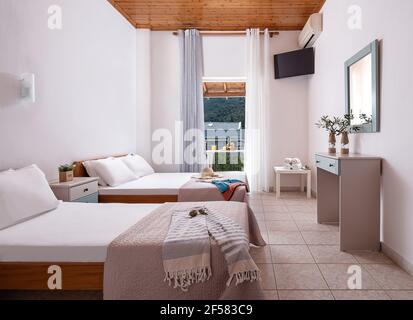 Weißes Interieur des Apartment-Schlafzimmer mit Einzel-, Doppel-King-Size-Bett. Familienzimmer mit Holzdecke, Fliesenboden, offener Tür, Country Vie Stockfoto