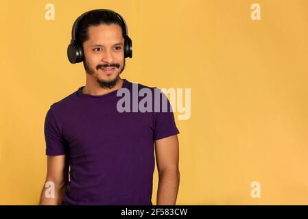 Junger Mann hört Musik mit Kopfhörern. Gelber Hintergrund. Stockfoto