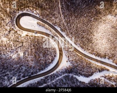 High-Angle-Luftaufnahme Drohne Bild auf der gebogenen Serpentin Straße durch die Bäume und Wald in Bergkette mit Weißer Schnee am Wintertag in der Nähe von Knja Stockfoto