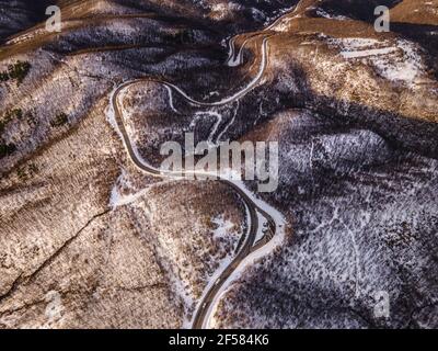 High-Angle-Luftaufnahme Drohne Bild auf der gebogenen Serpentin Straße durch die Bäume und Wald in Bergkette mit Weißer Schnee am Wintertag in der Nähe von Knja Stockfoto